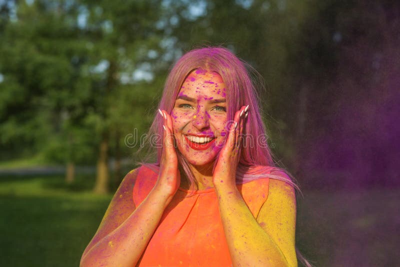 Lovely blonde girl having fun with colorful dry paint at the park. Concept for festival Holi. Lovely blonde woman having fun with colorful dry paint at the park royalty free stock images
